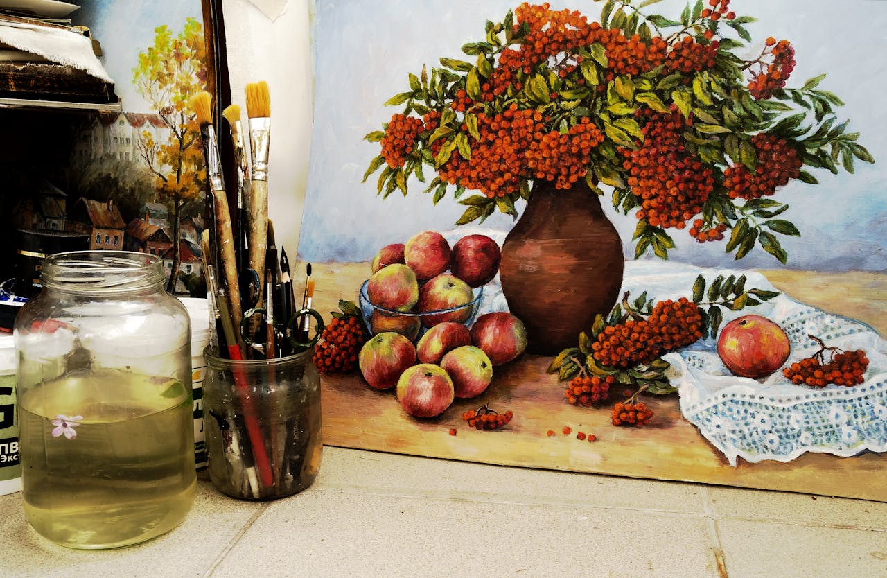 Still life painting with apples and berries beside a jar of paintbrushes.