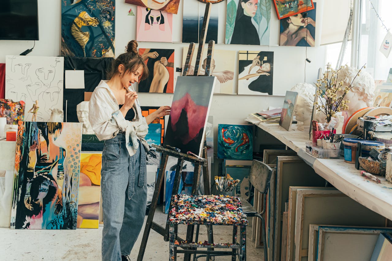 A young woman artist painting on canvas in her vibrant art studio filled with inspiring artworks.